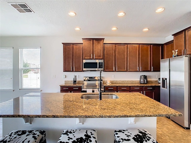 kitchen featuring a kitchen breakfast bar, stone counters, a textured ceiling, and appliances with stainless steel finishes