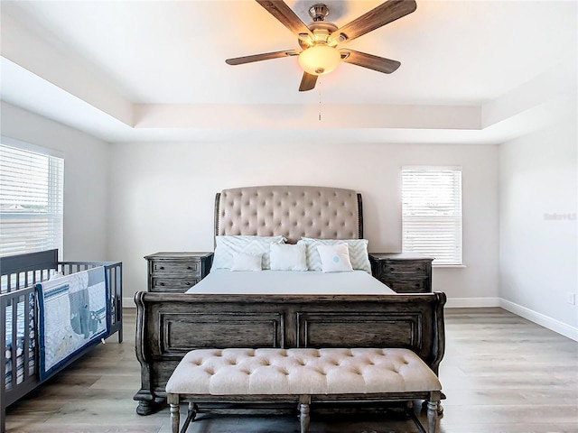 bedroom with hardwood / wood-style floors, ceiling fan, a raised ceiling, and multiple windows