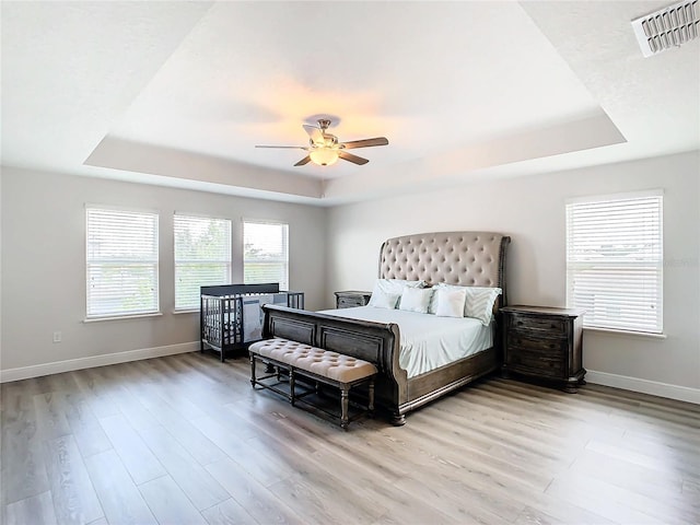 bedroom featuring hardwood / wood-style flooring, ceiling fan, a raised ceiling, and multiple windows