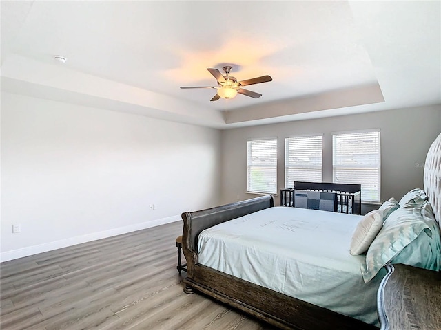 bedroom with hardwood / wood-style floors, a raised ceiling, and ceiling fan