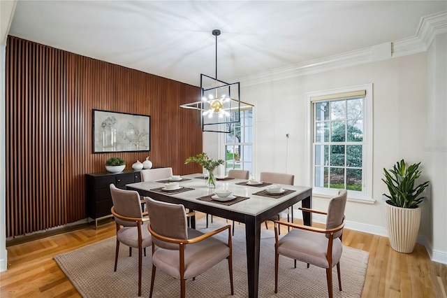 dining area with wooden walls, baseboards, ornamental molding, light wood-style floors, and a chandelier