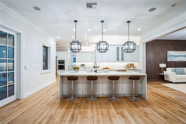 kitchen with light countertops, hanging light fixtures, glass insert cabinets, white cabinets, and a kitchen bar