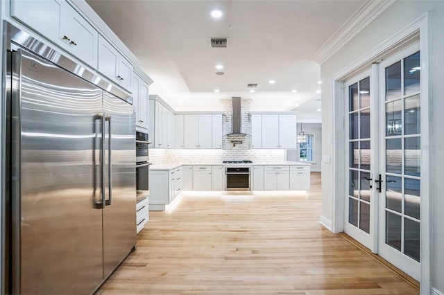 kitchen with stainless steel appliances, light countertops, wall chimney range hood, and white cabinetry