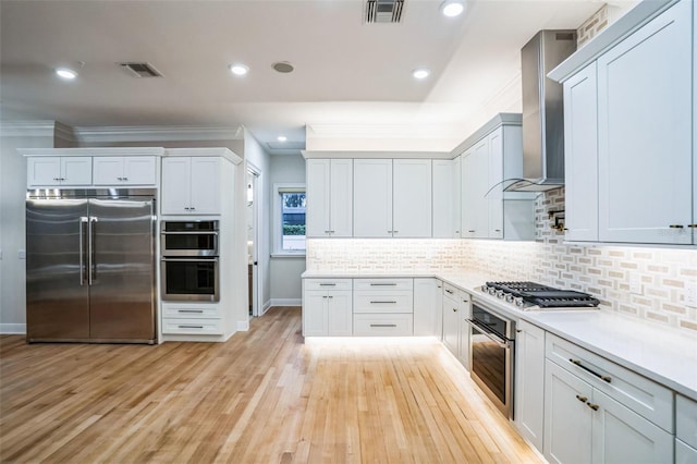 kitchen featuring stainless steel appliances, visible vents, white cabinetry, light countertops, and wall chimney range hood