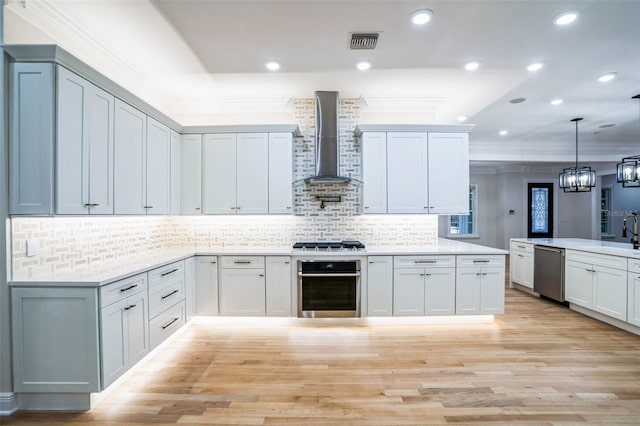 kitchen featuring visible vents, light countertops, wall chimney range hood, hanging light fixtures, and appliances with stainless steel finishes