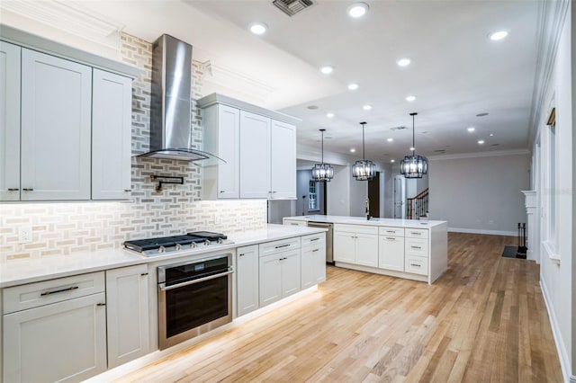 kitchen with visible vents, wall chimney exhaust hood, appliances with stainless steel finishes, ornamental molding, and hanging light fixtures