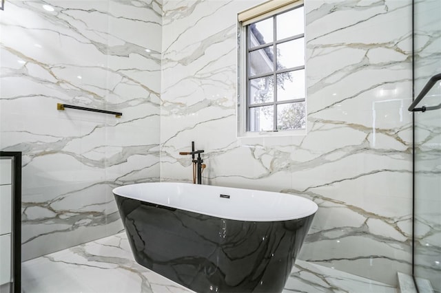 bathroom with stone wall, marble finish floor, and a freestanding bath