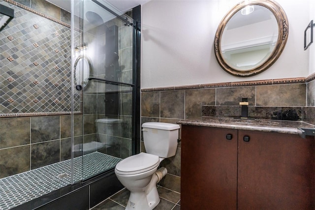 bathroom featuring toilet, a wainscoted wall, vanity, tile walls, and a stall shower