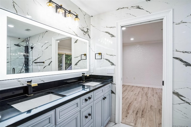 full bathroom featuring double vanity, a marble finish shower, a sink, and wood finished floors