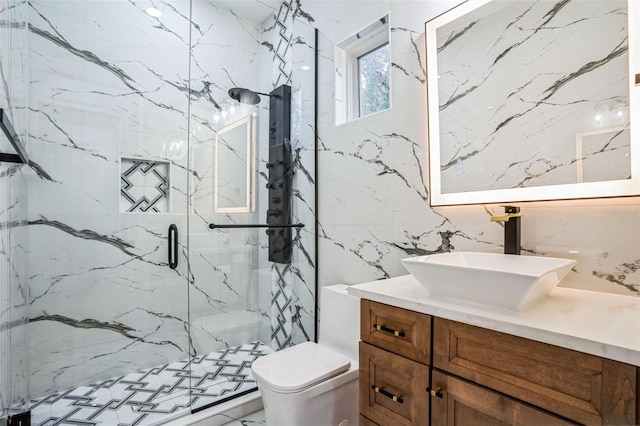 bathroom with tile walls, a marble finish shower, vanity, and toilet