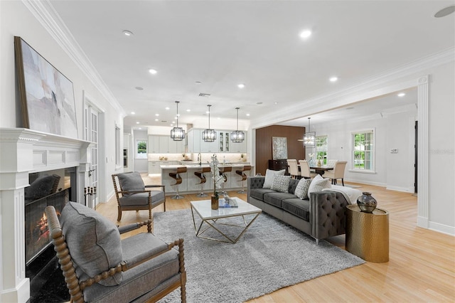 living room featuring a chandelier, a high end fireplace, light wood-style flooring, ornamental molding, and recessed lighting