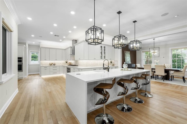 kitchen with crown molding, a sink, wall chimney exhaust hood, tasteful backsplash, and plenty of natural light