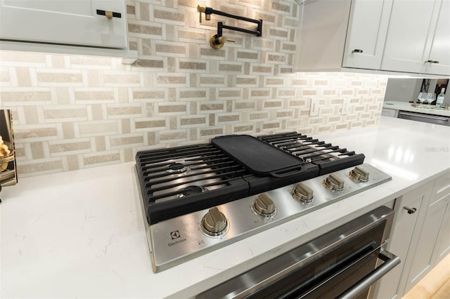 room details featuring stainless steel gas cooktop, backsplash, white cabinets, and light stone counters