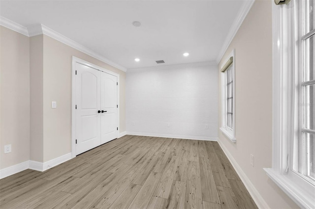 empty room featuring a wealth of natural light, crown molding, and light wood-type flooring