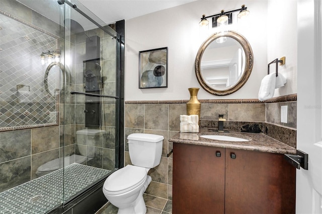 full bathroom with vanity, tile walls, toilet, a shower stall, and wainscoting