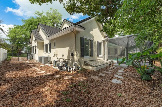 rear view of property featuring fence, central AC unit, glass enclosure, a fenced in pool, and stucco siding