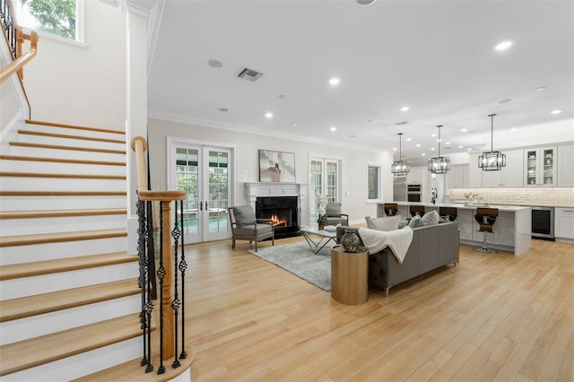 living room featuring stairway, a lit fireplace, wine cooler, light wood-style floors, and visible vents
