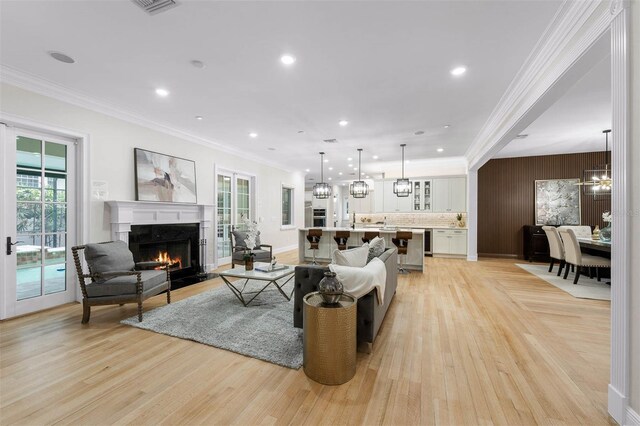 living room with a fireplace, recessed lighting, ornamental molding, and light wood finished floors