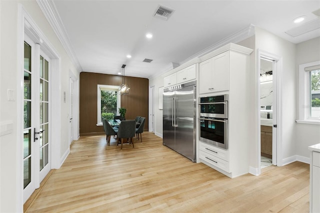 kitchen featuring crown molding, white cabinetry, light wood-type flooring, stainless steel appliances, and visible vents