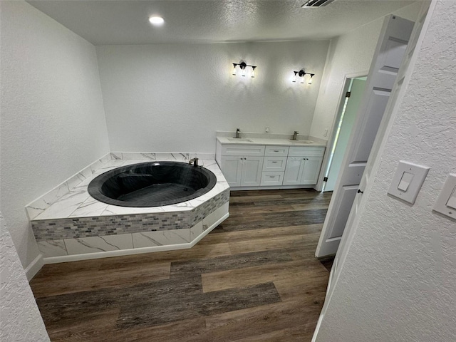 bathroom featuring hardwood / wood-style flooring, vanity, tiled tub, and a textured ceiling