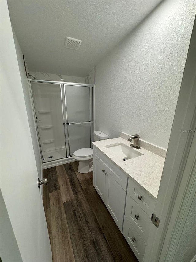 bathroom featuring vanity, wood-type flooring, a textured ceiling, toilet, and walk in shower