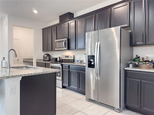 kitchen featuring stainless steel appliances, sink, light stone counters, light tile patterned floors, and dark brown cabinetry