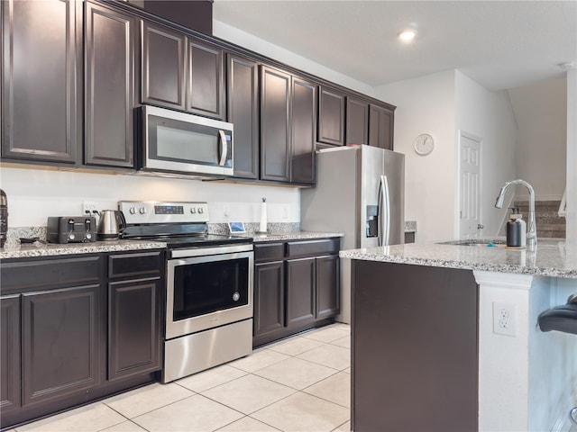 kitchen with appliances with stainless steel finishes, light stone counters, dark brown cabinetry, sink, and light tile patterned flooring