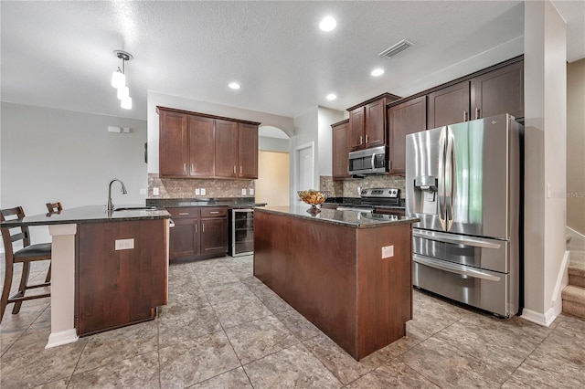 kitchen featuring sink, hanging light fixtures, beverage cooler, an island with sink, and appliances with stainless steel finishes