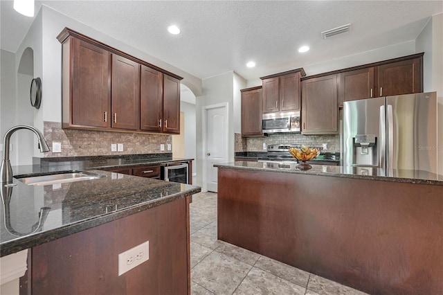 kitchen featuring appliances with stainless steel finishes, a textured ceiling, dark brown cabinetry, sink, and dark stone countertops