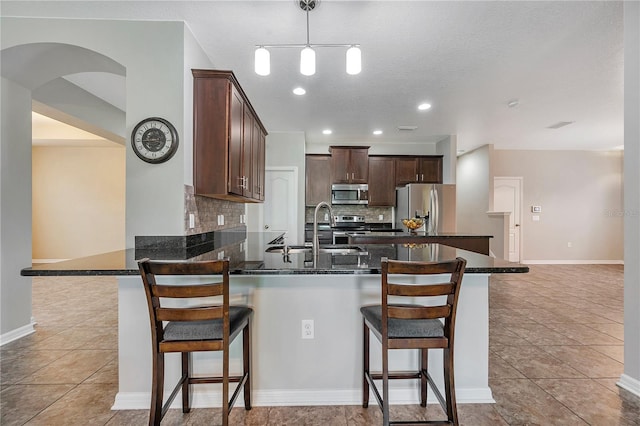 kitchen featuring backsplash, stainless steel appliances, sink, hanging light fixtures, and a breakfast bar area