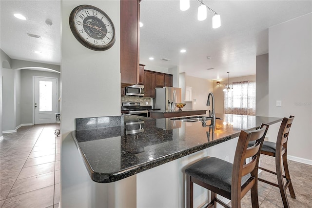 kitchen with dark stone counters, kitchen peninsula, pendant lighting, and stainless steel appliances