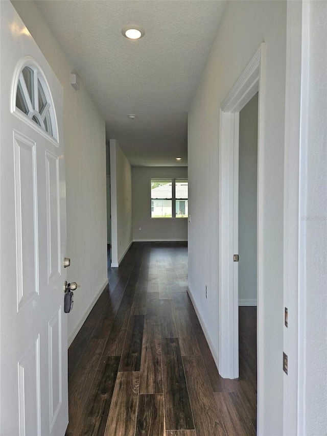 corridor with a textured ceiling and dark hardwood / wood-style floors