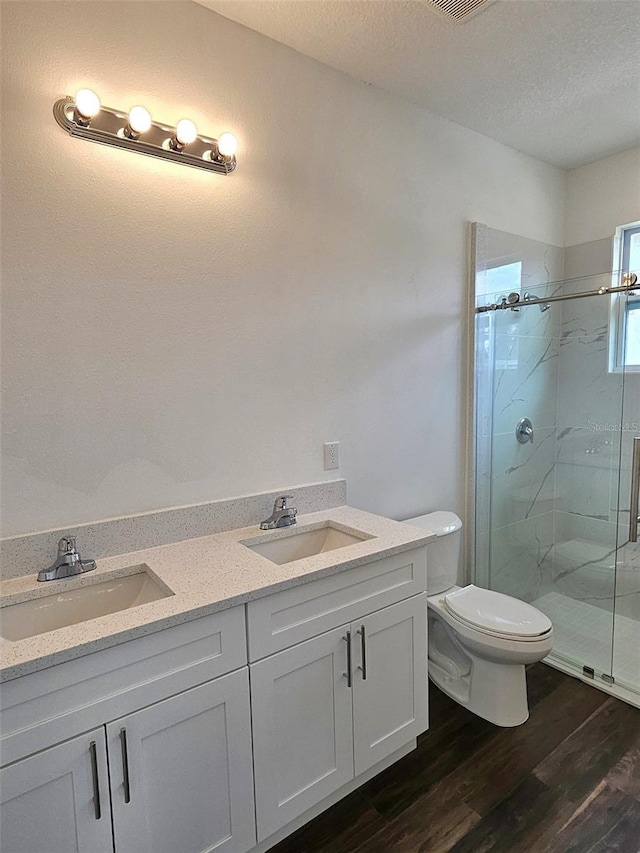 bathroom featuring vanity, a textured ceiling, a shower with door, hardwood / wood-style flooring, and toilet