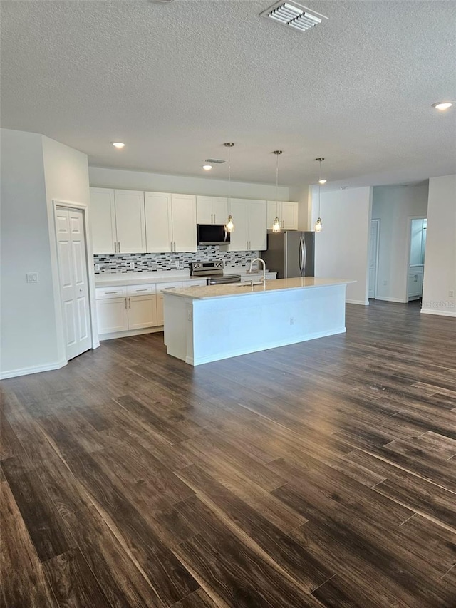 kitchen with backsplash, stainless steel appliances, decorative light fixtures, a center island with sink, and white cabinets