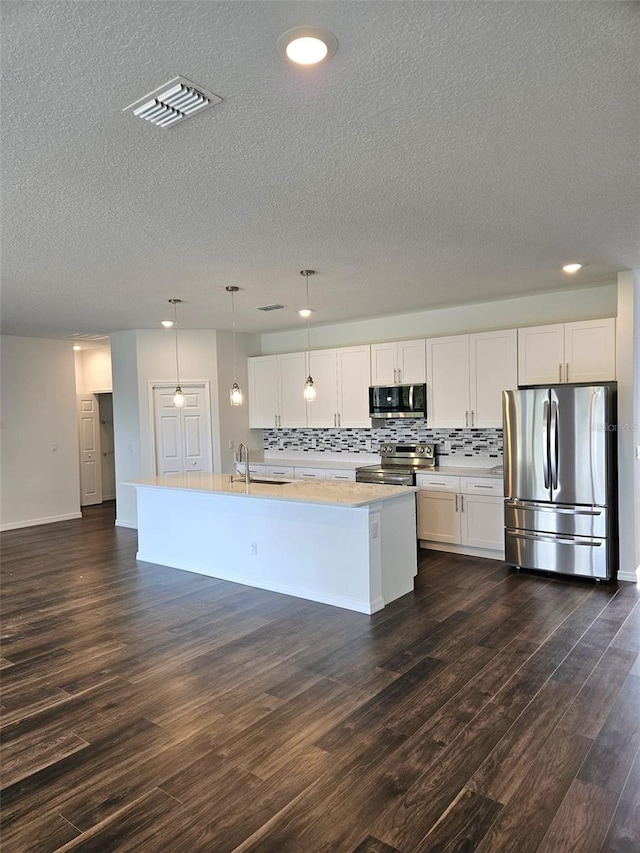 kitchen with white cabinetry, hanging light fixtures, appliances with stainless steel finishes, and an island with sink