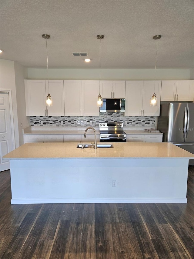 kitchen featuring decorative light fixtures, white cabinetry, stainless steel appliances, and an island with sink