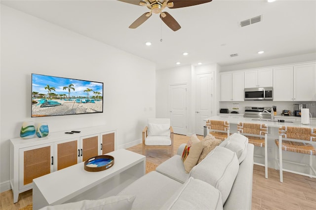 living room with light hardwood / wood-style flooring, ceiling fan, and sink