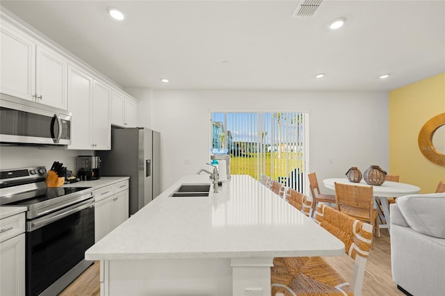 kitchen featuring a kitchen island with sink, white cabinets, sink, light hardwood / wood-style floors, and stainless steel appliances