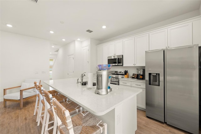 kitchen with stainless steel appliances, white cabinetry, light hardwood / wood-style floors, and an island with sink