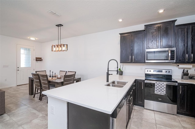 kitchen with pendant lighting, sink, a textured ceiling, a kitchen island, and stainless steel appliances