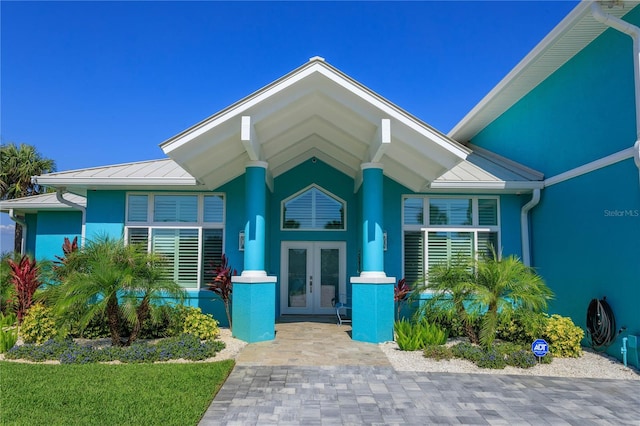 view of exterior entry with a standing seam roof, french doors, stucco siding, and metal roof