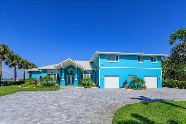 view of front of home with french doors, decorative driveway, a garage, a front lawn, and stucco siding