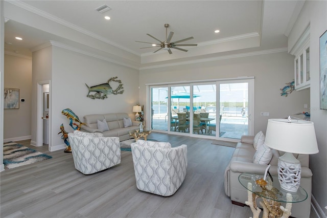 living room featuring a tray ceiling, crown molding, ceiling fan, and light wood-type flooring