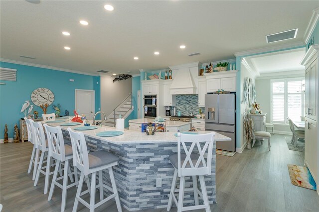 kitchen featuring appliances with stainless steel finishes, a spacious island, custom exhaust hood, ornamental molding, and recessed lighting