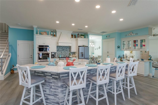 kitchen featuring white cabinetry, a large island, a breakfast bar, custom range hood, and appliances with stainless steel finishes