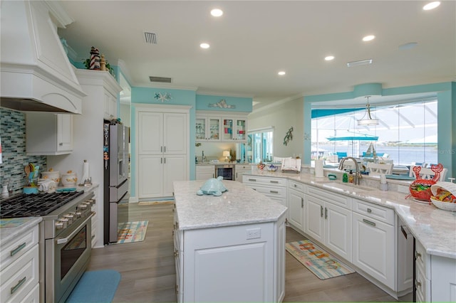 kitchen featuring a center island, appliances with stainless steel finishes, white cabinets, custom range hood, and ornamental molding