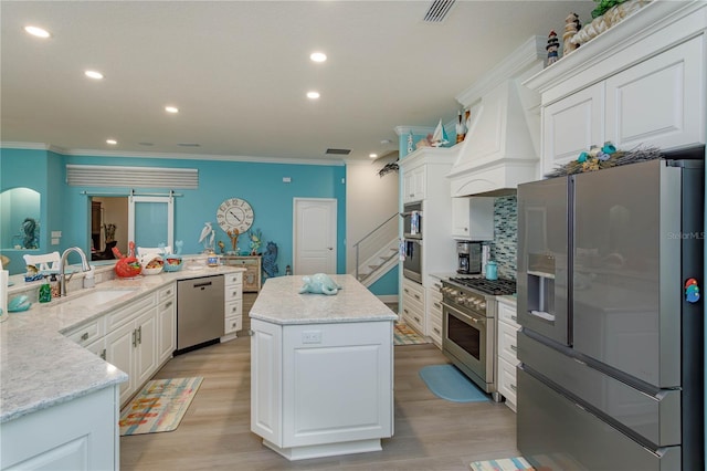 kitchen with appliances with stainless steel finishes, a sink, a center island, ornamental molding, and white cabinets