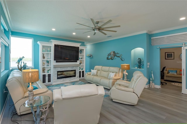 living room with light wood-type flooring, ceiling fan, ornamental molding, and a premium fireplace