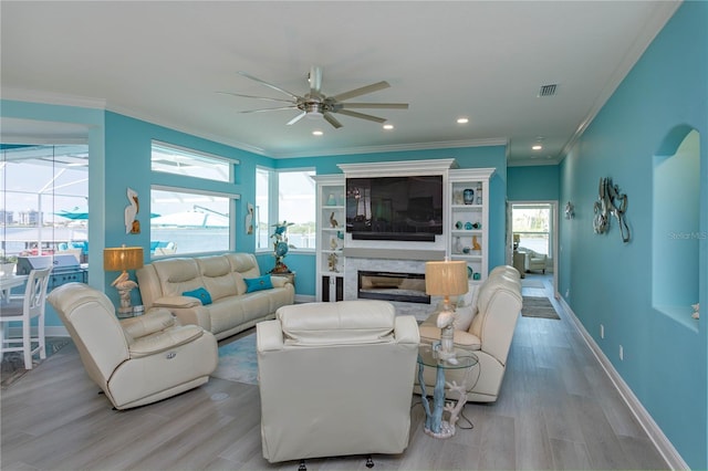 living area featuring ceiling fan, light wood-type flooring, crown molding, a glass covered fireplace, and baseboards