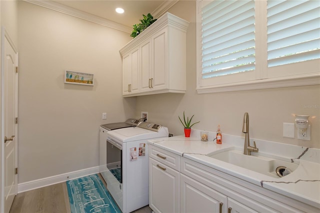 clothes washing area with cabinet space, washing machine and dryer, baseboards, light wood-style flooring, and ornamental molding